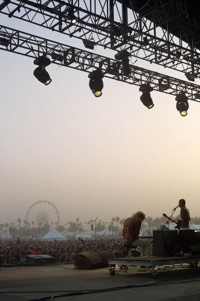 two men playing instruments on stage in front of a crowd at an outdoor music festival