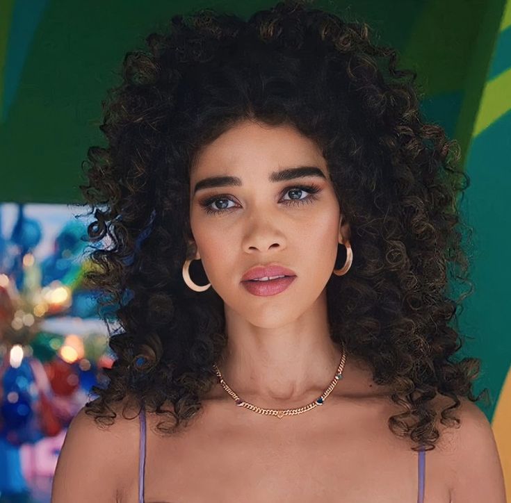 a woman with curly hair wearing a purple bra and gold hoop earrings is looking at the camera