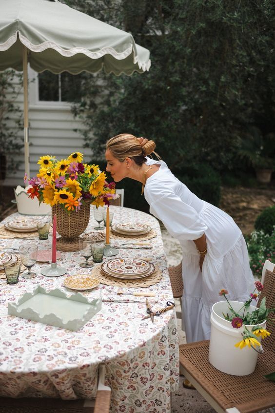 a woman standing over a table with plates and cups on it in front of an umbrella