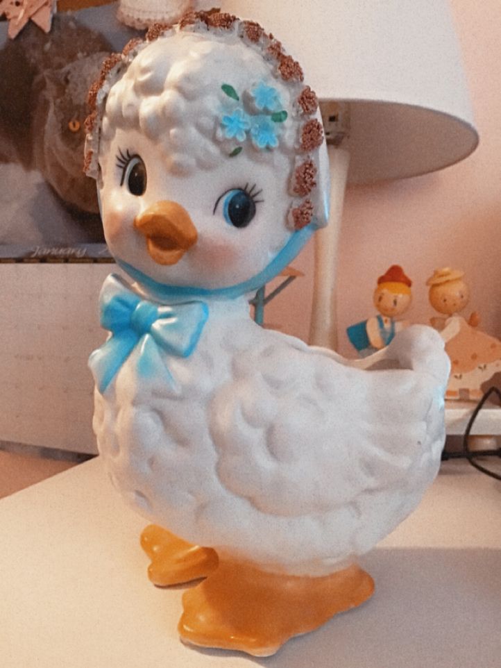 a white duck figurine sitting on top of a table next to a lamp