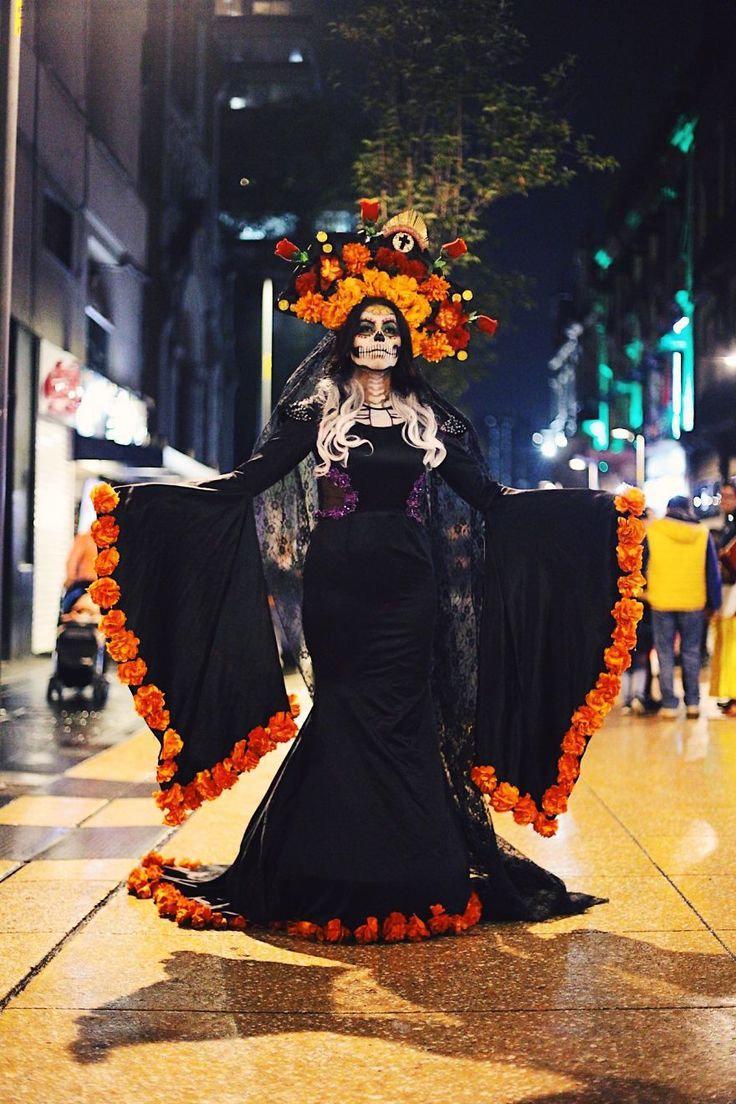 a woman dressed up as a skeleton with flowers on her head and dress in the street