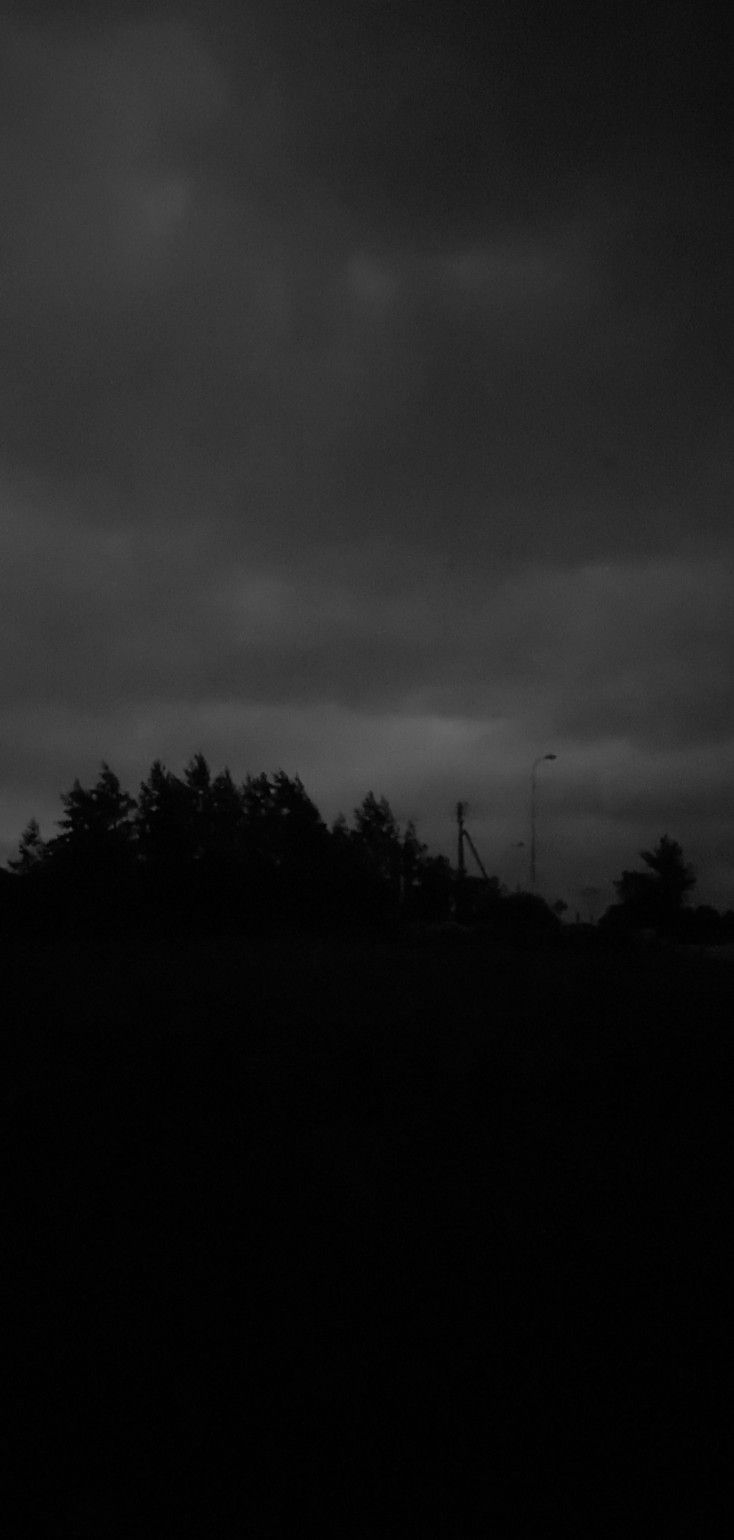 a black and white photo of the sky with dark clouds in the background, as well as trees