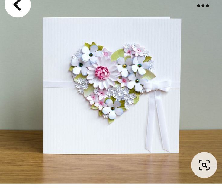 a white card with flowers in the shape of a heart on top of a wooden table