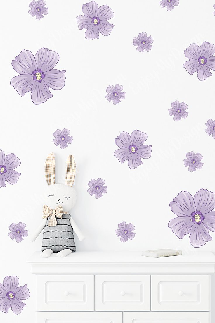 a white dresser sitting next to a wall with purple flowers on it and a stuffed bunny