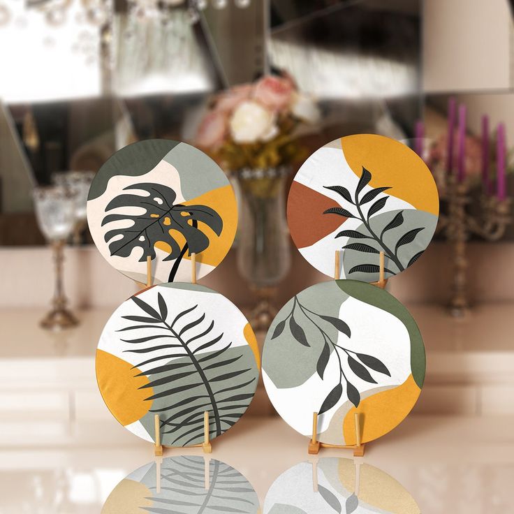 three decorative discs with plants on them sitting on a table in front of a mirror