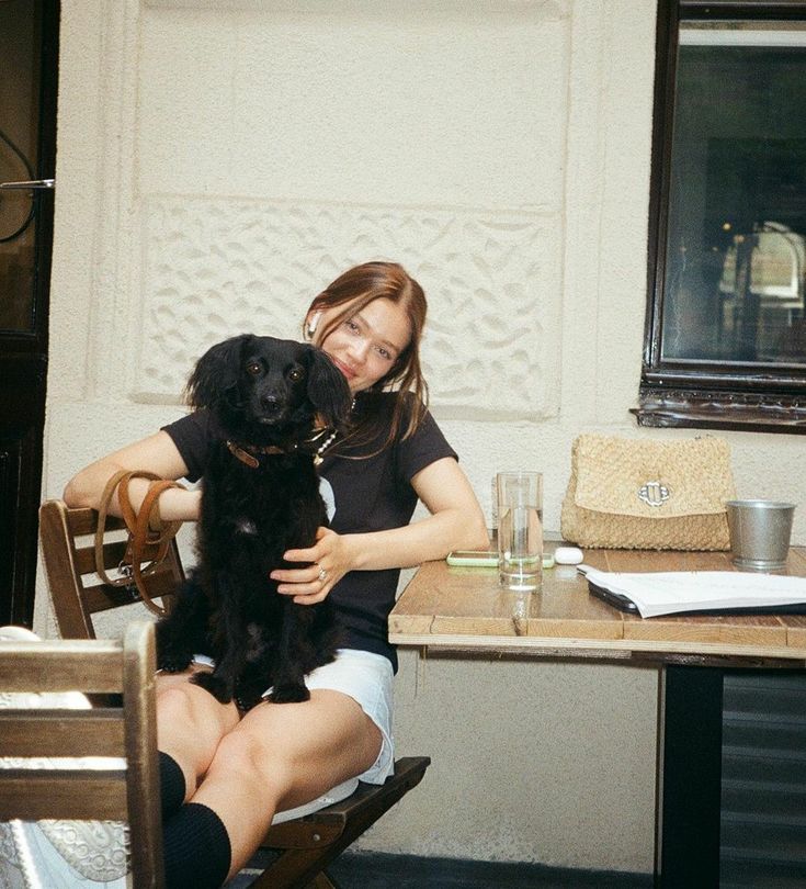 a woman sitting at a table with her dog in front of her and holding it