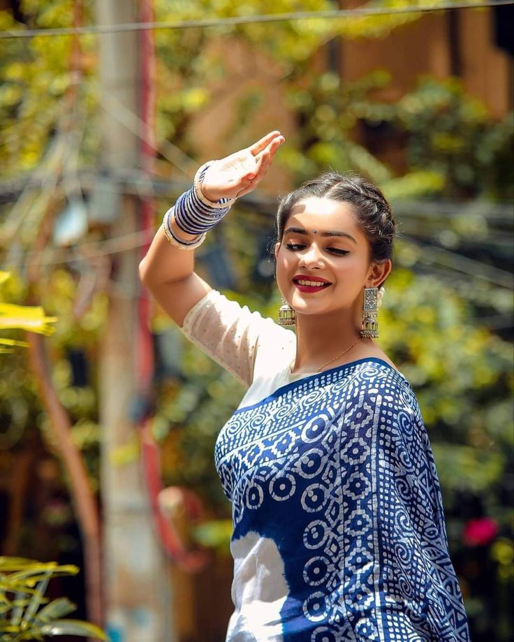 a woman in a blue and white sari waving to the side with her hand