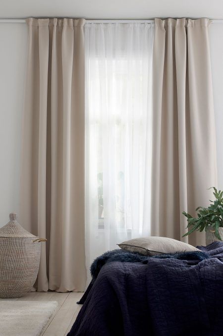 a bed sitting next to a window with curtains on it's sides and a potted plant in the corner