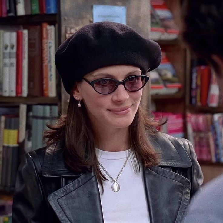 a woman wearing sunglasses and a hat in front of a book shelf with books on it