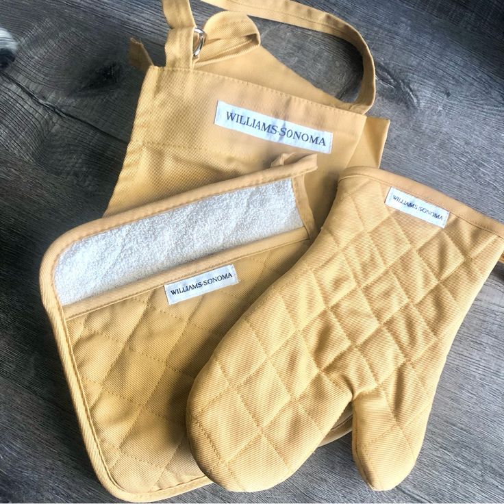 two oven mitts with labels on them sitting next to each other in front of a wooden table