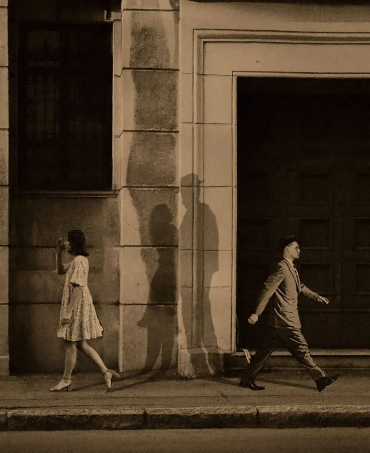 a man and woman walking down the street in front of an open door with shadows on it