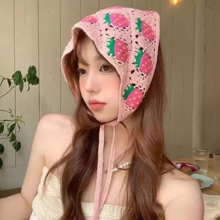 a woman with long hair wearing a pink crochet hat and necklace, looking at the camera