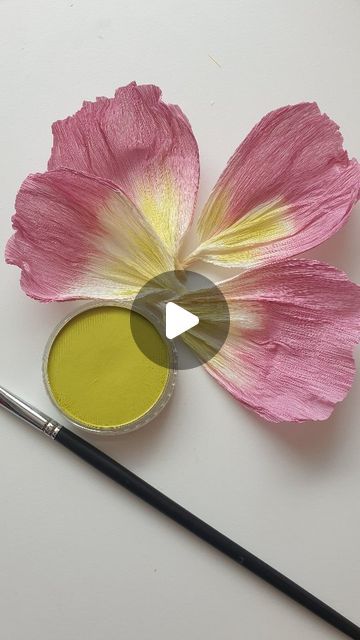 a pink flower sitting on top of a white table next to a paint roller and a brush