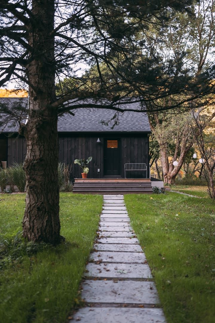 a path leading to a small cabin in the woods with trees and grass on either side