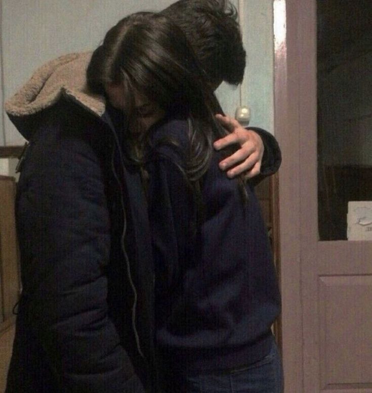 two people standing next to each other in front of a door with their arms around one another