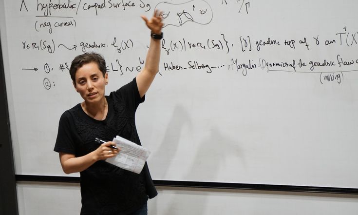 a man standing in front of a whiteboard with writing on it and holding his hand up