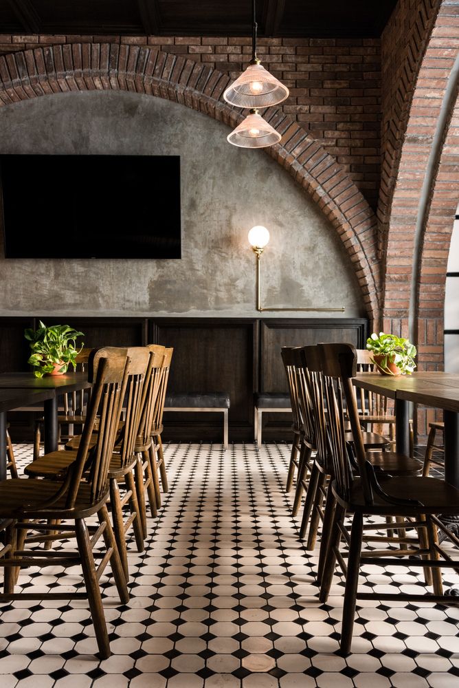 a restaurant with black and white tile flooring and wooden chairs in front of a flat screen tv mounted on the wall