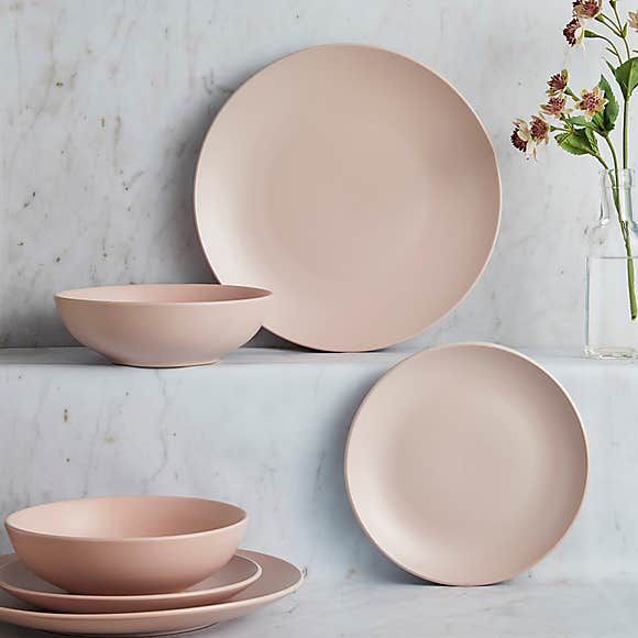 three plates and two bowls on a marble surface with flowers in vases behind them