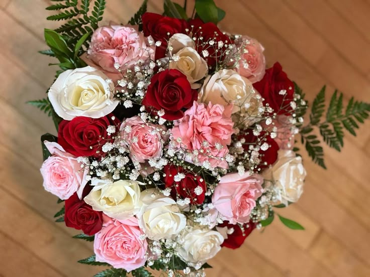 a bridal bouquet with red, white and pink flowers on a wooden table top