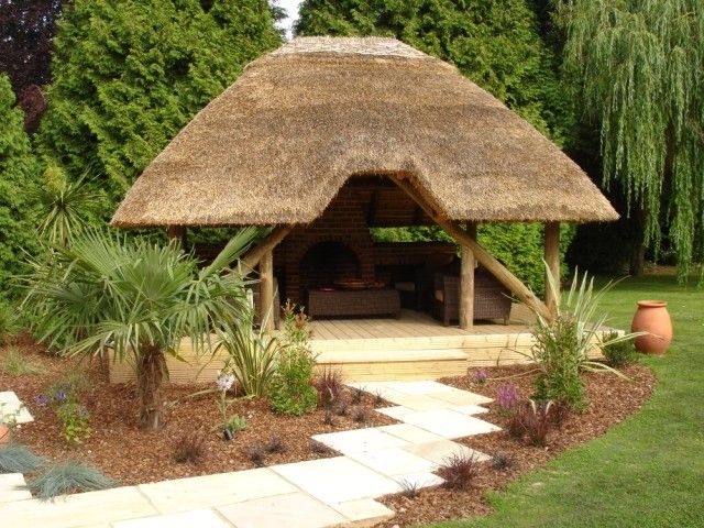 a thatched roof gazebo in the middle of a garden