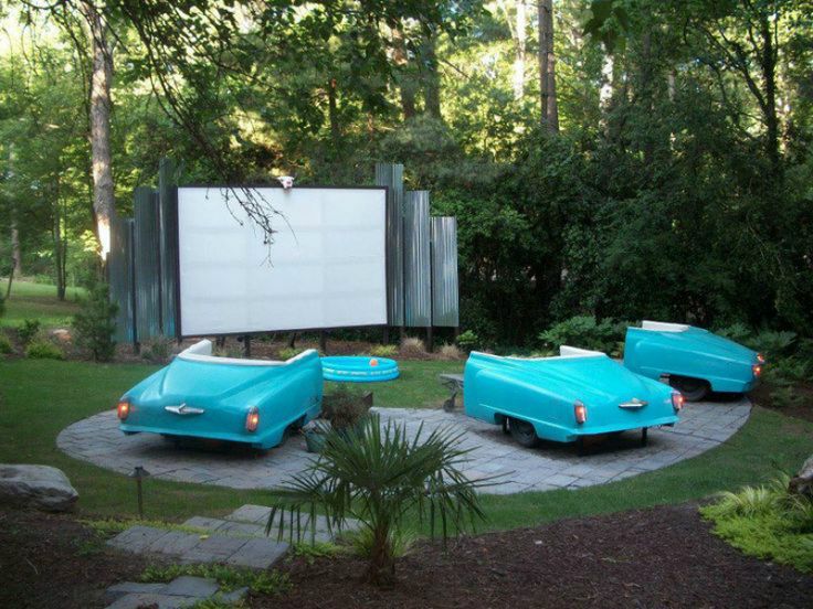 three blue cars are parked in front of a movie screen and some trees on the other side