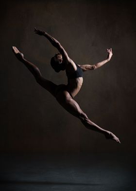 a male ballet dancer in the air with his arms extended and legs spread out,