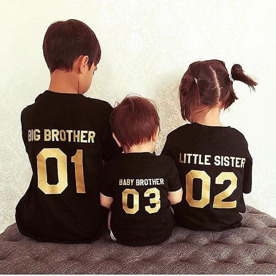 three children in matching shirts sitting on a bed