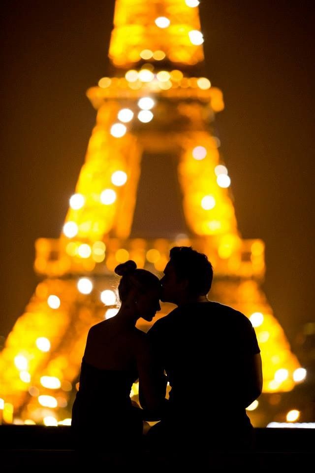 two people standing next to each other in front of the eiffel tower at night