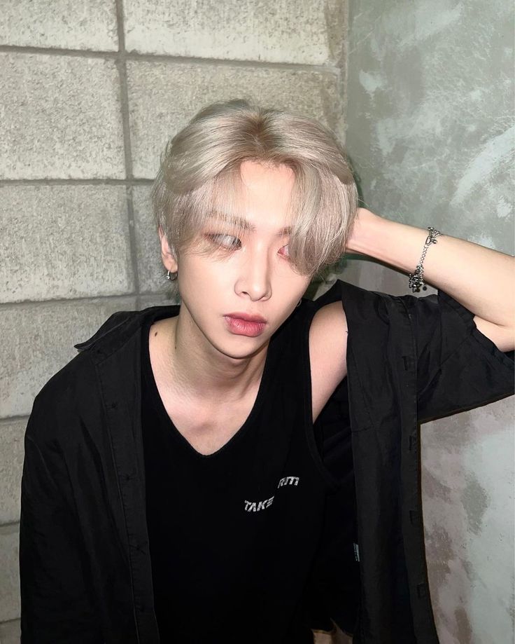 a young man with blonde hair and piercings on his ears sitting in front of a brick wall