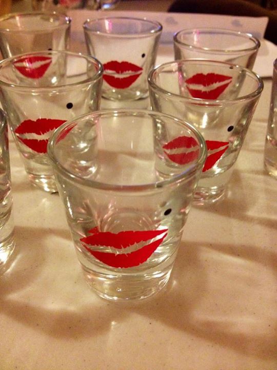 many glasses with red lipstick painted on them sitting on a white tablecloth covered table