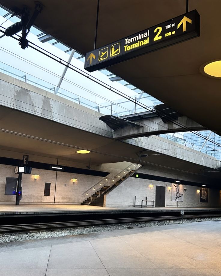 an empty train station with stairs leading up to the platform and exit sign above it