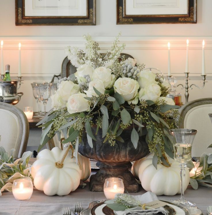 a dining room table is set with white flowers and pumpkins, candles and plates