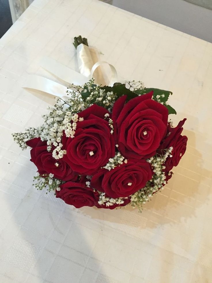 a bouquet of red roses and baby's breath on a table with white ribbon