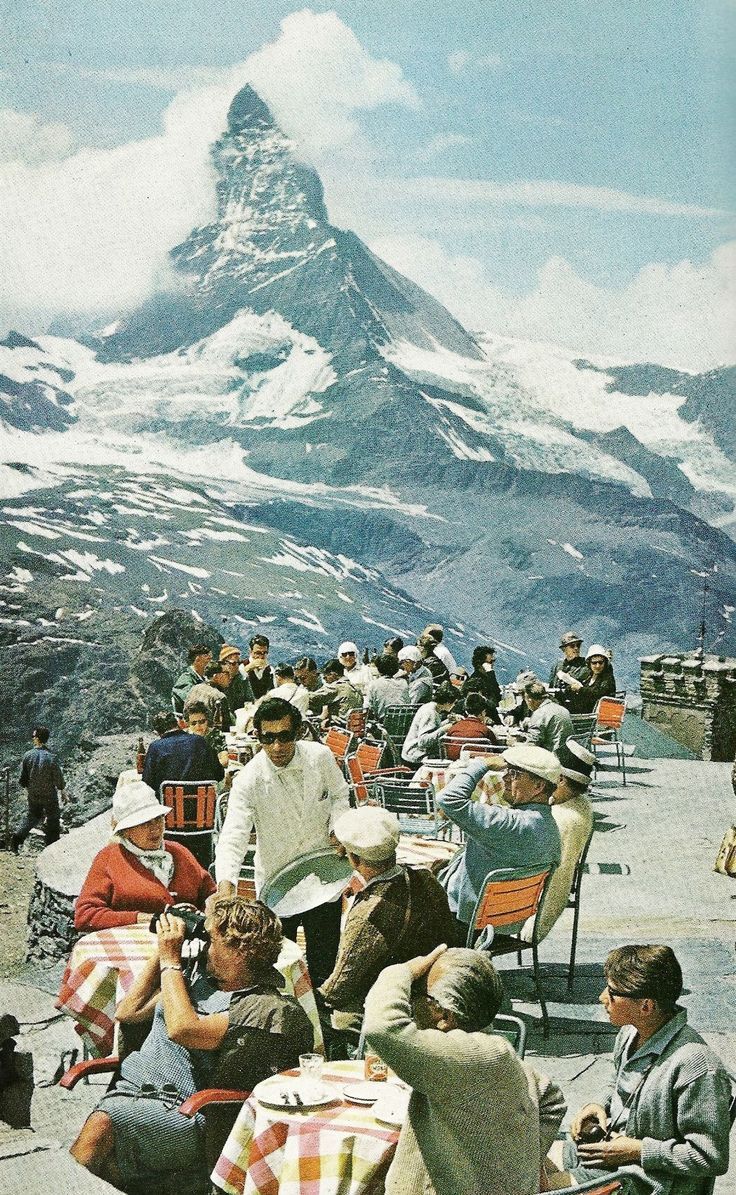 many people are sitting in chairs on the top of a mountain with a snow covered peak behind them