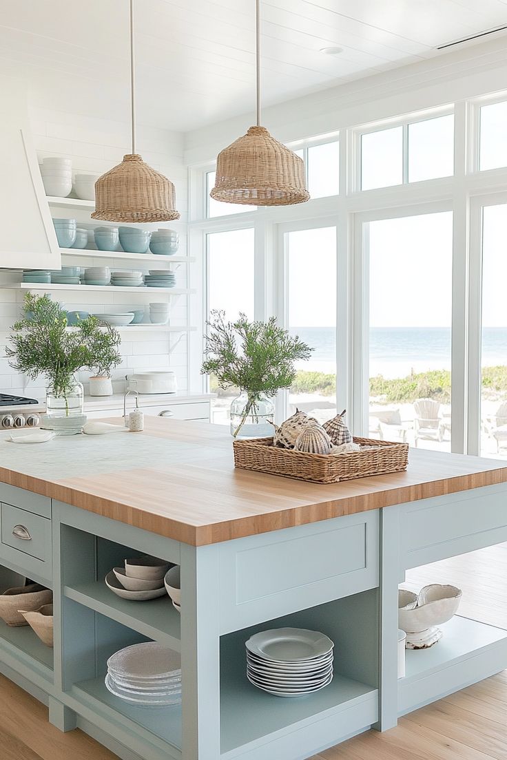 a kitchen island with plates and bowls on it in front of large windows overlooking the ocean