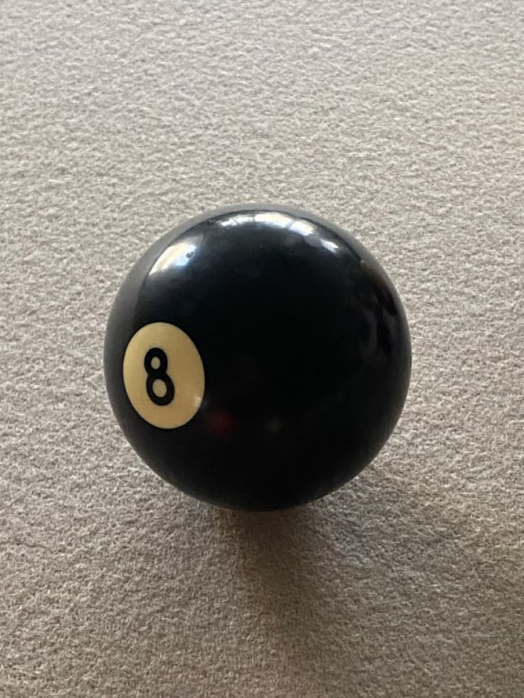 a black pool ball with the number 8 on it's side sitting on a white carpet