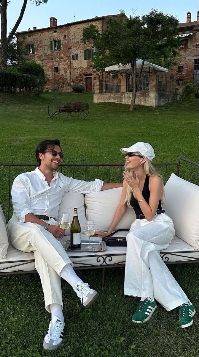 a man and woman sitting on top of a white couch next to each other in the grass