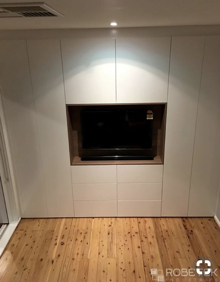 an empty room with wood flooring and white cupboards on the wall, in front of a window