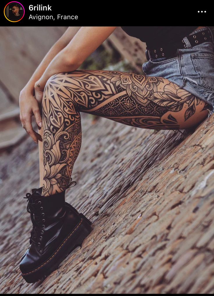 a person sitting on top of a rock next to a wall with tattoos on their legs