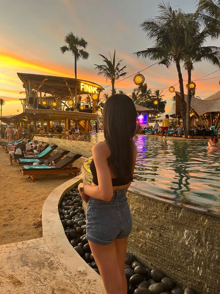 a woman standing in front of a pool at sunset