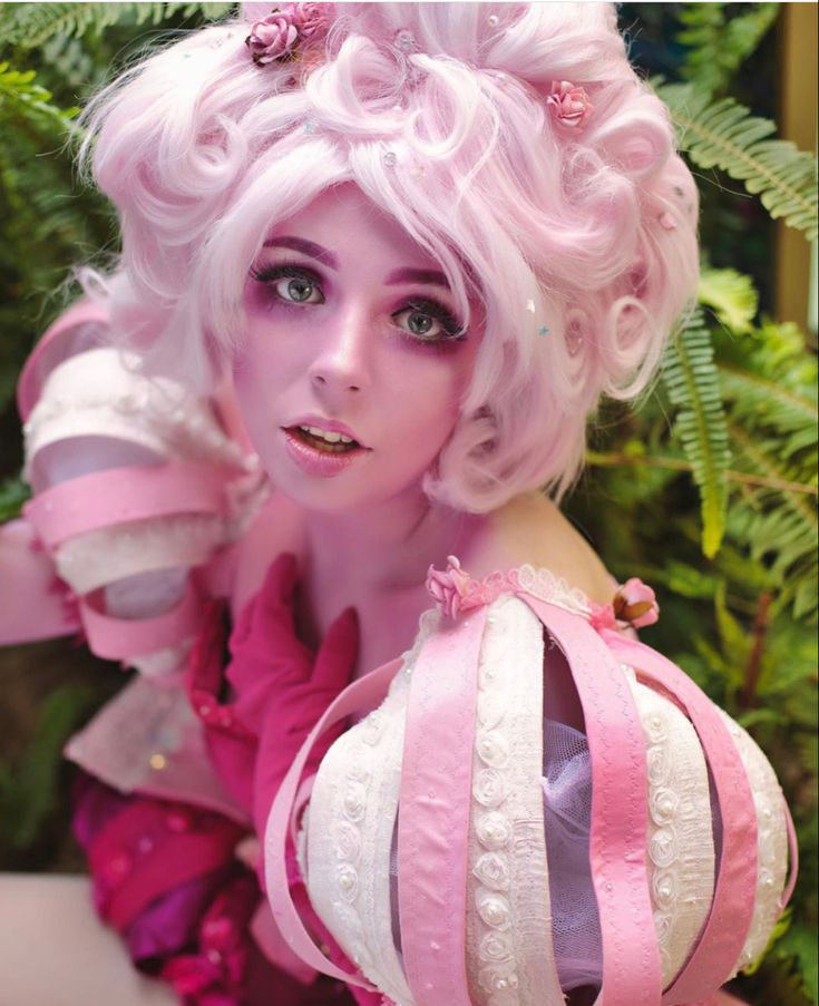 a close up of a person wearing pink and white hair with flowers in the background