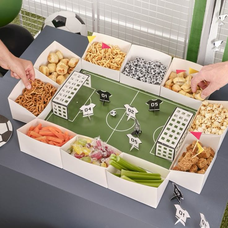 two hands reaching for food in front of a football field cutout on a table