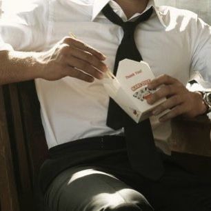 a man sitting down reading a book with his hands on his lap and wearing a tie