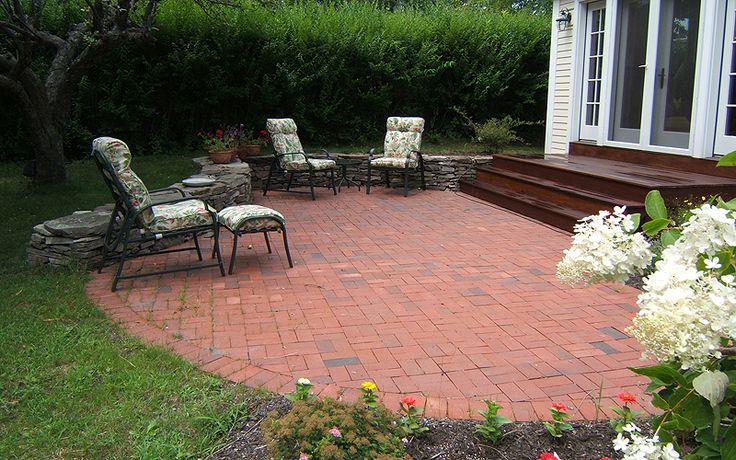 a brick patio with chairs and flowers in the foreground