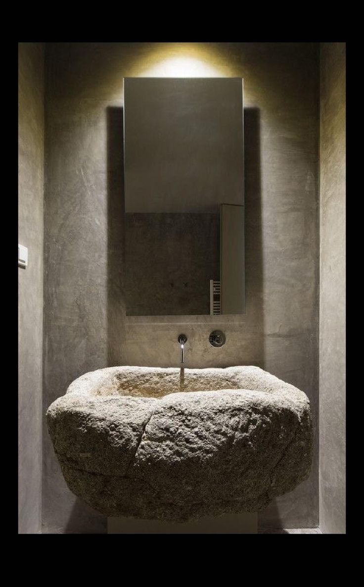 a stone sink in the corner of a room with a mirror above it and lights on