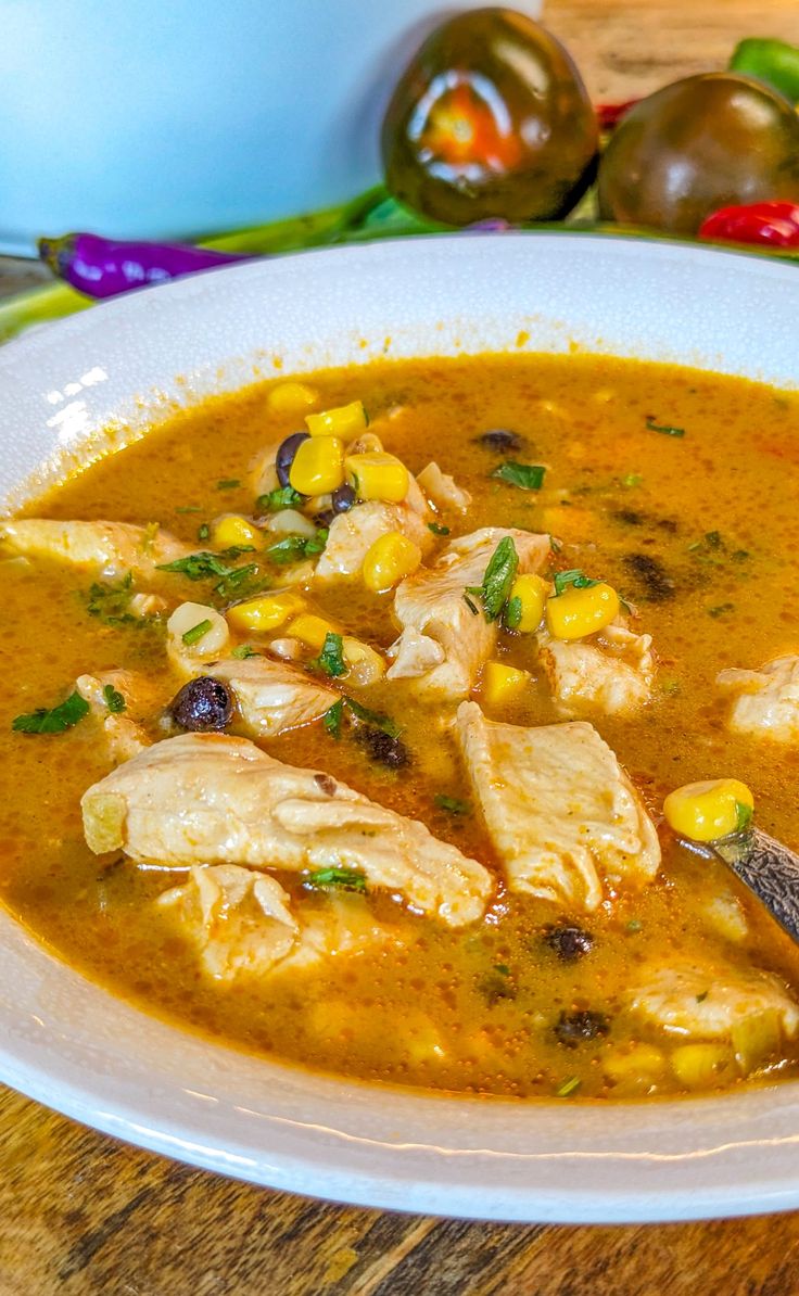 a white bowl filled with chicken and corn soup on top of a wooden table next to a spoon