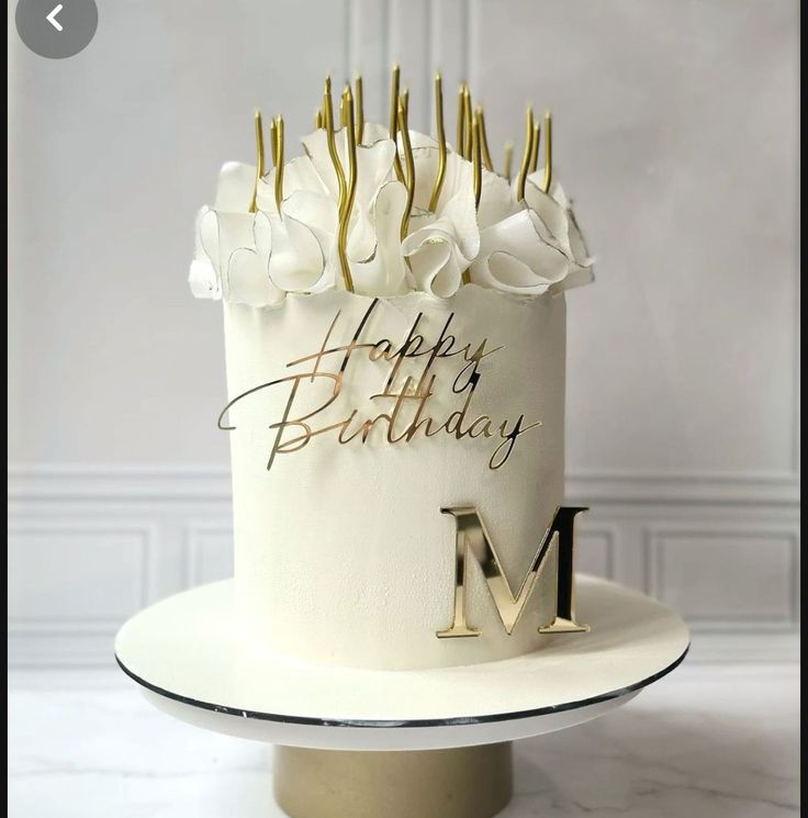 a birthday cake with white flowers and gold letters on the top is decorated with an m