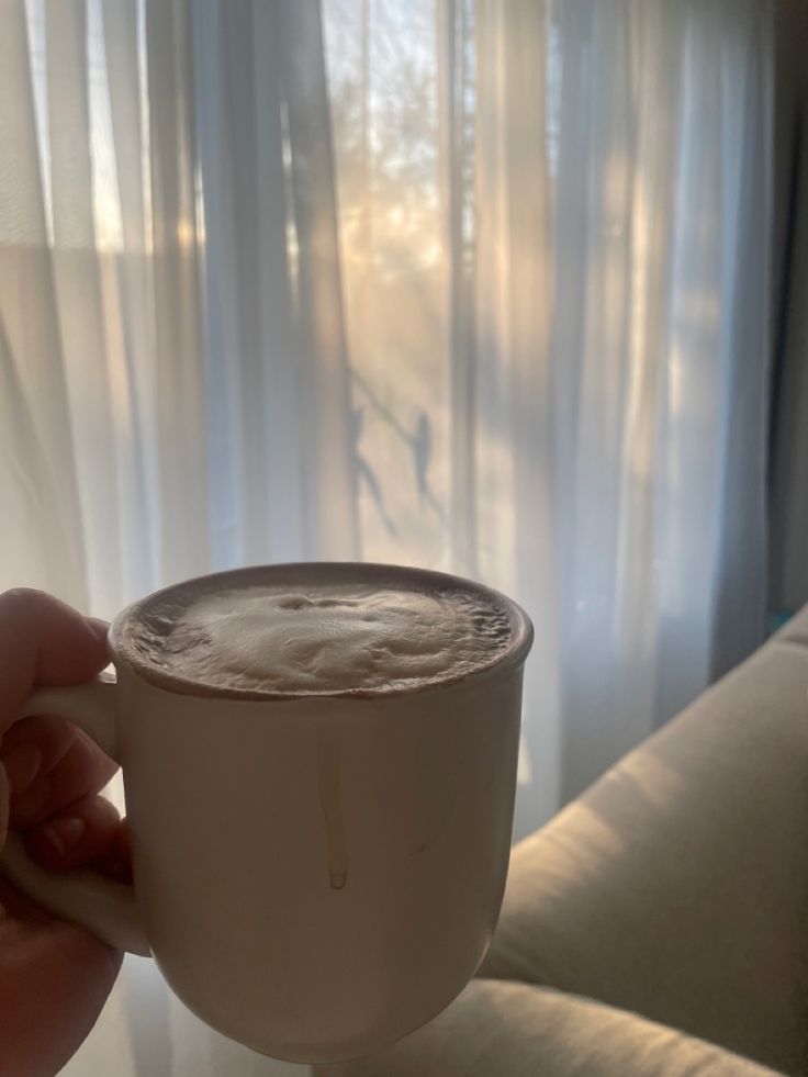 a person holding a coffee cup in front of a window