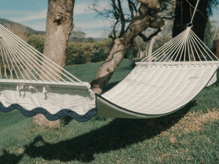 two white hammocks sitting in the grass next to a tree