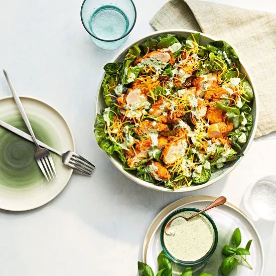 a salad in a bowl with dressing on the side and two glasses next to it